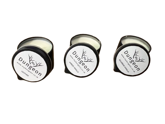 Three small round candles in black metal tins with white lids are shown on a plain white background. All are open, revealing pale cream wax.