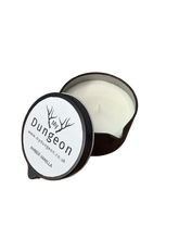 Load image into Gallery viewer, An open black scented candle tin with white wax, shown on a plain white background. The lid is placed beside the tin and printed with the brand name 'My Dungeon'