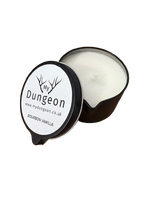 Load image into Gallery viewer, An open black metal candle tin showing white wax inside, with the lid placed beside it. The lid label reads 'My Dungeon' and 'Bourbon Vanilla'.
