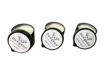Load image into Gallery viewer, Three small round candles in black metal tins with white lids are shown on a plain white background. All are open, revealing pale cream wax.